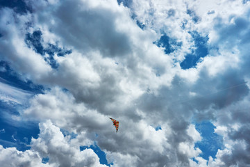 A large kite floats high in the sky among the clouds against the blue sky and the bright summer sun and it is controlled by two white ropes going to the ground