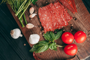 Smoked salami on a black table and a brown board. Sausages with rosemary, garlic and pepper and tomato cherry, dill, parsley