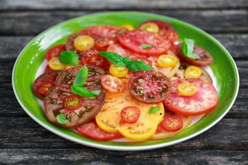 Colorful Tomato Salad with heirloom, pear shaped, beef heart, tigerella, brandywine, cherry, black tomatoes in a green plate. healthy food