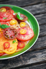 Colorful Tomato Salad with heirloom, pear shaped, beef heart, tigerella, brandywine, cherry, black tomatoes in a green plate. healthy food