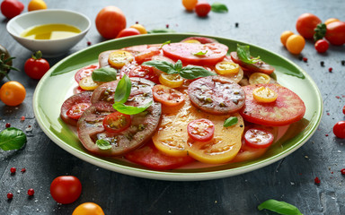 Colorful Tomato Salad with heirloom, pear shaped, beef heart, tigerella, brandywine, cherry, black tomatoes in a green plate. healthy food