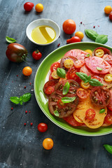 Colorful Tomato Salad with heirloom, pear shaped, beef heart, tigerella, brandywine, cherry, black tomatoes in a green plate. healthy food