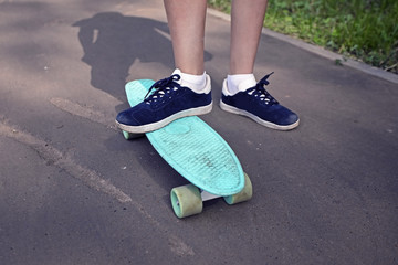 skateboard with the feet of a teenager in sneakers on the asphalt road