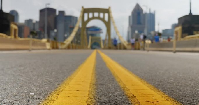 A low angle slow dolly tracking shot of the bridgedeck of the Roberto Clemente Bridge in downtown Pittsburgh, Pennsylvania. City skyline in the distance.  	