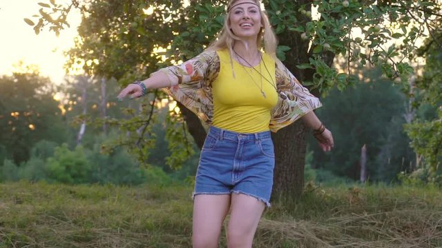 young attractive woman in a yellow T-shirt is spinning at sunset. green apple orchard on background. happy and free hippies slowmotion HD