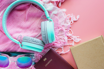 Headphones with passport, notebook, sunglasses and scarf on pink background for travel concept. Flat lay and top view image.