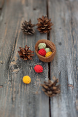 Knitted berries in a basket and natural cones on a wooden background