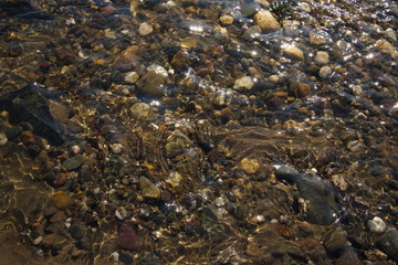 Various size and color of pebble and round stones under shallow clear flowing and streaming water in the canal and river 