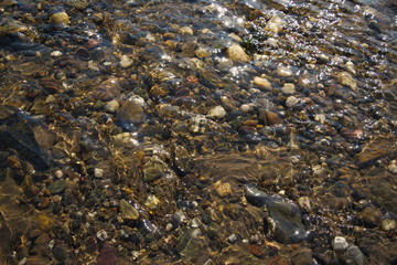 Various size and color of pebble and round stones under shallow clear flowing and streaming water in the canal and river 