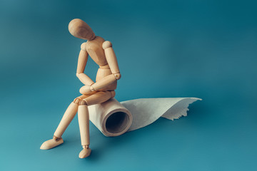 Wooden figure sit on a roll of toilet paper. Concept of the problem with digestion.