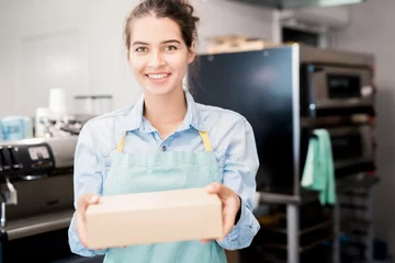 Foto op Canvas Waist up  portrait of smiling young  woman wearing apron holding box with takeaway food and looking at camera, copy space © Seventyfour