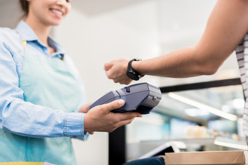 Low angle close up of unrecognizable woman paying via smart watch in local bakery, copy space