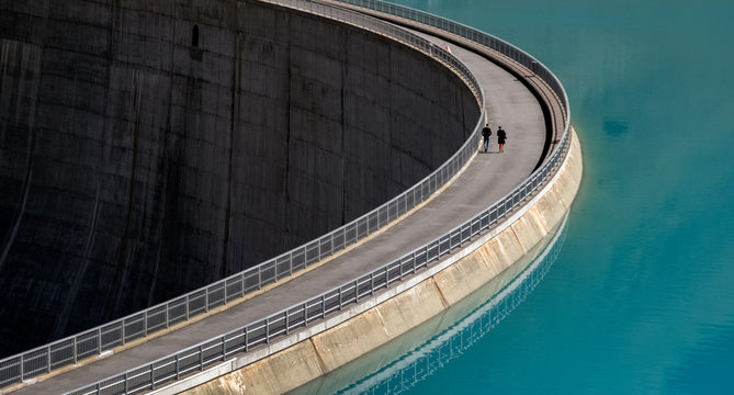 Two people taking a stroll on a sunny autumn afternoon on the dam wall of the Moiry Reservoir. (Valais, Switzerland)