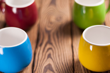Four colored empty ceramic clean mugs on old worn brown wooden table