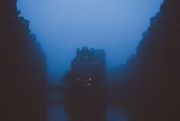 Obraz premium Famous panorama of Speicherstadt, warehouse district in Hafen city in Hamburg, Germany. Gray dense fog covering shady red bricked buildings and canal water. Vintage retro colors