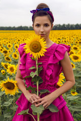 woman in a pink dress standing in the field with sunflowers