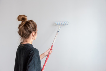 Young woman paints a wall with a roller in a new apartment during a renovation.