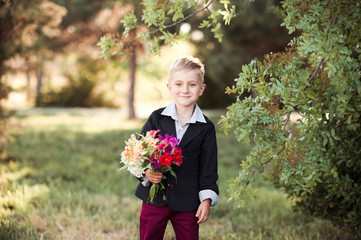 Fototapeta premium Smiling pupil boy holding flowers and wearing school uniform outdoors. Looking at camera. Back to school.