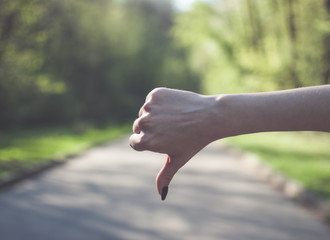 Girl making a thumbs down (dislike) gesture against sunny green background.