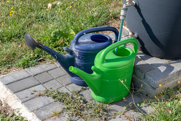 Two watering cans at the rain barrel for filling