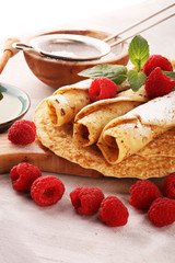 Homemade crepes served with fresh raspberrries and powdered sugar on rustic table.