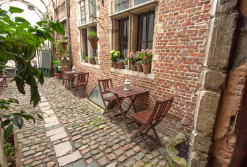 Fototapeta na wymiar Wooden tables for hungry visitors of cozy outdoor cafe in old style narrow street, with brick walls and cobbled stones