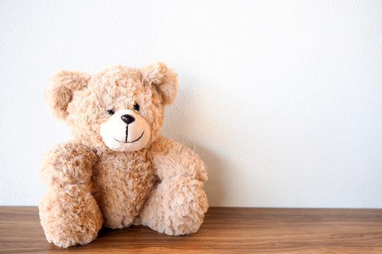 Cute Teddy Bear sitting alone with white wall on wooden table