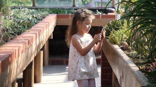Child little girl takes mobile phone pictures of variety of cactus plants in a greenhouse of the botanical garden