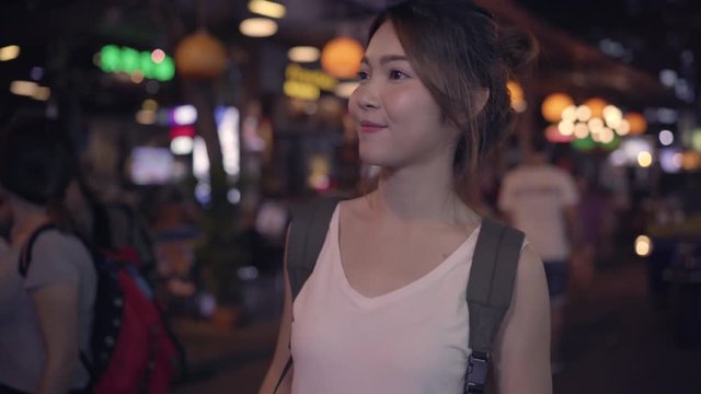Traveler backpacker asian woman travel in Khao San road at Bangkok, Thailand. Happy young female spending holiday trip at amazing landmark and enjoy her journey traditional city in the night.