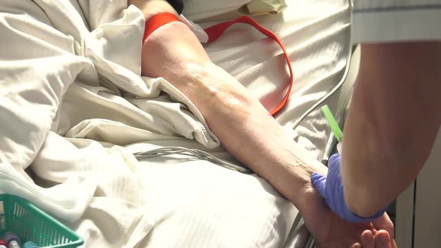 An elderly man lies on a bed in a hospital. Tubes drip in hand.Peripheral venous catheter in hand. Panning camera, Pan, Closeup