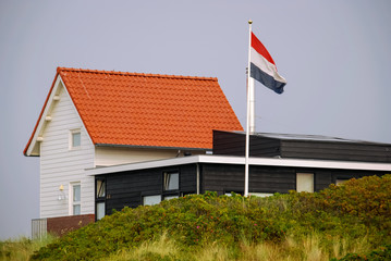Fototapeta na wymiar A white house and the Dutch flag on the Frisian Island of Vlieland, The Netherlands. The Frisian Islands, are also known as the Wadden Islands or Wadden Sea Islands