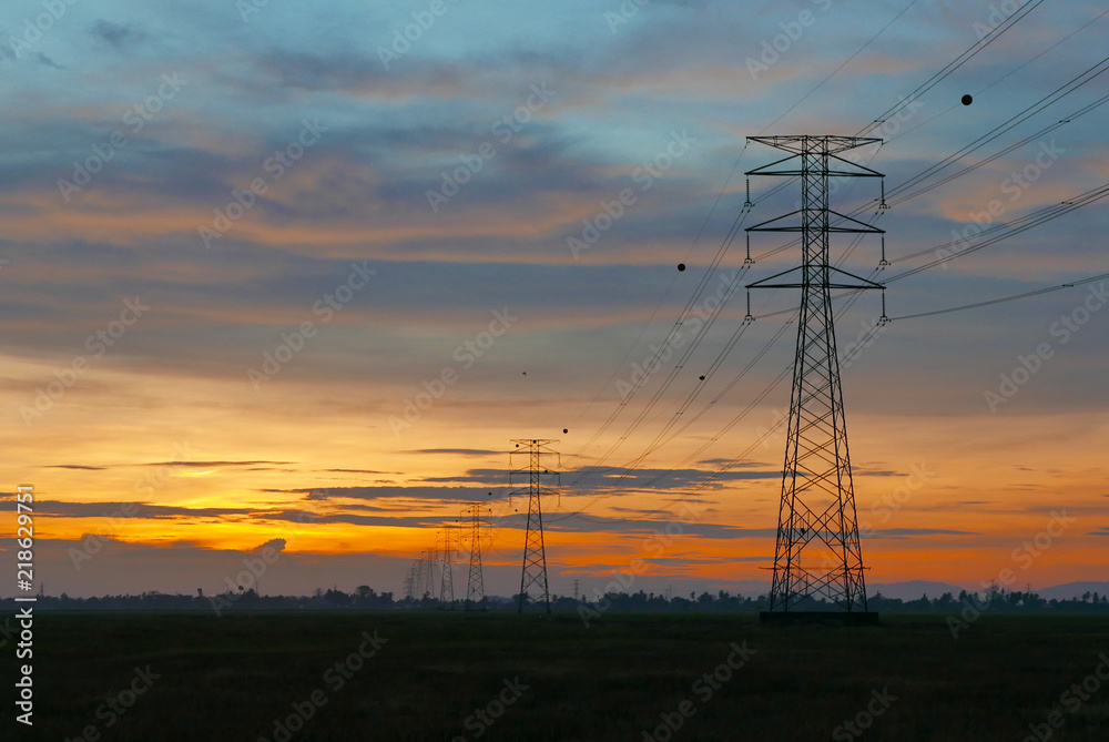 Wall mural sunset over electricity pylon on a paddy field at a village.