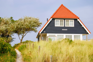 Obraz premium A blue house and the Dutch flag on the Frisian Island of Vlieland, The Netherlands. The Frisian Islands, also known as the Wadden Islands or Wadden Sea Islands