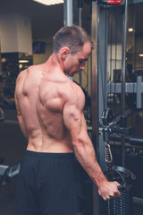 Portrait of a strong mature athletic man bodybuilder working out at the gym performing rope pushdown exercise on his triceps