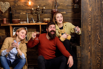 Friends spend leisure in cozy interior. Man and ladies on happy faces discussing and drinking mulled wine. Communication concept. Friends have fun, speaking and drinking hot drinks in wooden interior