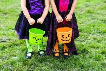 Two little girls hold an orange and green jack o lantern trick or treat candy buckets