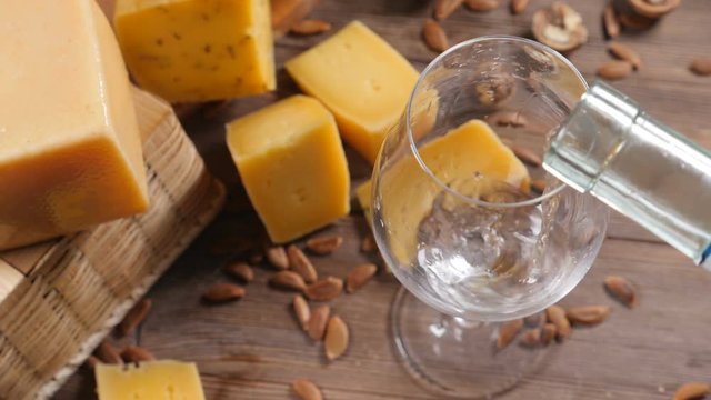 Wine and cheese. Food art. Different sorts of hard cheese beautifully surved on a wooden background. White wine is being poured into wine glass.