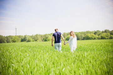 Fototapeta premium A young couple walking hand in hand through the field