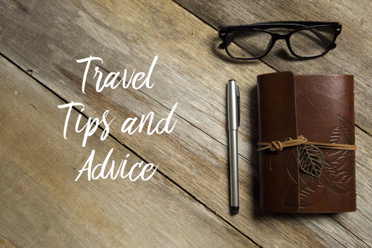 Top view of eyeglasses,pen and notebook on wooden background written with TRAVEL TIPS AND ADVICE.
