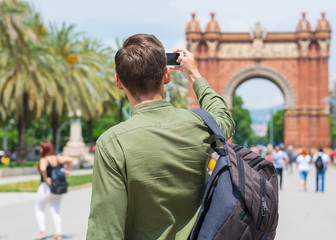 A young guy, tourist, takes pictures with a smartphone near the Arc de Triomf in Barcelona, Spain.