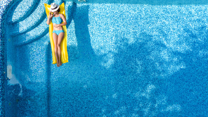 Beautiful young girl relaxing in swimming pool, swims on inflatable mattress and has fun in water on family vacation, tropical holiday resort, aerial top view from above
