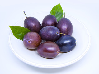 Ripe delicious plums in white plate on a white background. Plum with leaves.