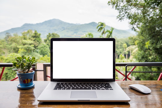 blank screen of laptop with mouse and  plant vase on wooden table, Mountain and forest background