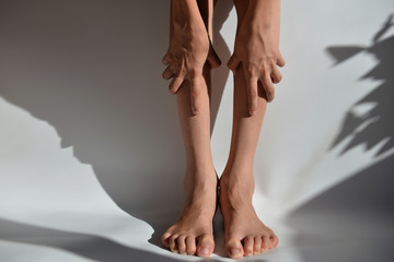 Hands and feet of a young man on a white background with a shadow. Hands clasp their legs