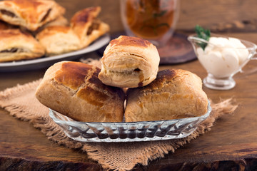 Sweet dessert-puff pastry with cheese filling in a plate on a linen napkin, gravy boat with sour cream, a glass of herbal tea, all on a wooden background.