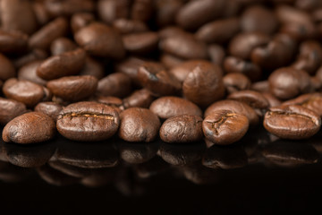 Close up pile of Coffee beans with reflection on glossy black materail