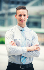 Portrait of Handsome Businessman Posing with Crossed Arms and Smiling in Urban Background