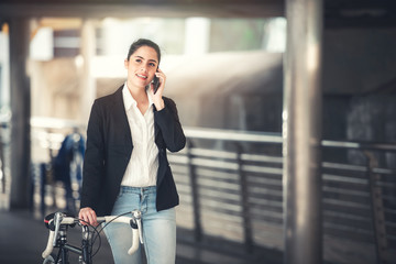 Fototapeta premium Attractive Smart Businesswoman Using Smartphone with Smile with Her Bicycle on Urban Street - Business and Lifestyle Concept