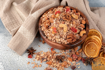 Wooden Bowl with granola with nuts, dried cranberries and dried orange on a old light table