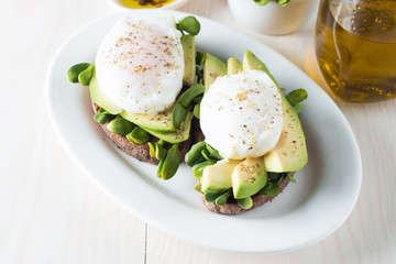 Avocado toast, cherry tomato on wooden background. Breakfast with toast avocado, vegetarian food, healthy diet concept. Healthy sandwich with avocado and poached eggs.